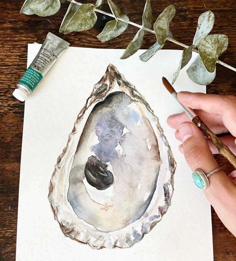 May include: Watercolor painting of an oyster shell with a pearl inside. The shell is painted in shades of gray, brown, and white. The pearl is a dark gray color.