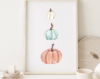 May include: A framed print with three watercolor pumpkins in a vertical line. The top pumpkin is white, the middle pumpkin is light blue, and the bottom pumpkin is peach.