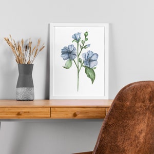 May include: A watercolor painting of blue flowers with green leaves and stems on a white background. The painting is framed in a white frame and is hanging on a white wall.