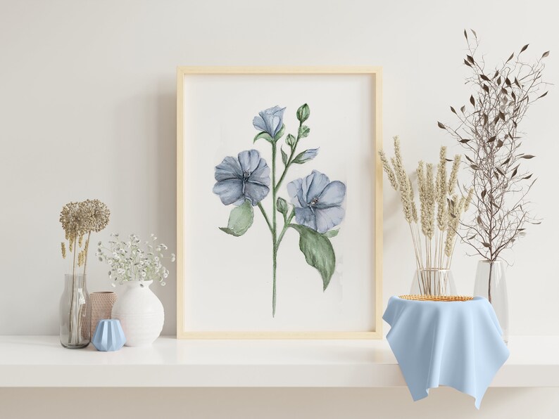 May include: A watercolor painting of blue flowers with green leaves in a light wood frame. The painting is on a white shelf with a vase of white flowers and a blue vase.