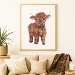 Könnte beinhalten: Gerahmter Aquarelldruck eines Highland-Kuhkalbes. Das Kalb hat zotteliges, rotbraunes Fell, kleine Hörner und einen sanften Ausdruck. Das Kunstwerk wird vor einem weißen Hintergrund präsentiert.