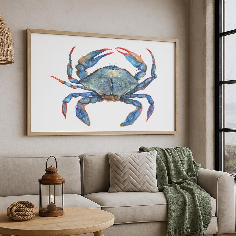 May include: A rectangular framed wall art piece featuring a watercolor illustration of a blue crab with distinct red-tipped claws and legs. The crab is centered on a white background, showcasing shades of blue, teal, and orange-red accents.