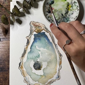 May include: A watercolor painting of an oyster shell with a blue, green, and brown color scheme. The shell is painted on a white background.