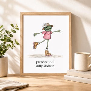 Könnte beinhalten: Ein gerahmter Kunstdruck mit einem grünen Frosch, der einen beigen Hut mit einer weißen Blume, ein rosa T-Shirt und braune Rollschuhe trägt. Der Frosch ist in einer Rollschuh-Pose dargestellt. Darunter steht der Text: professional dilly-dallier.