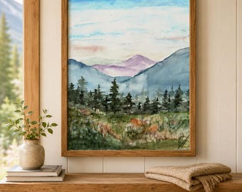Pode incluir: Uma pintura em aquarela emoldurada retratando uma paisagem com um primeiro plano de prado verde e flores silvestres, um plano médio de pinheiros verde-escuros e um fundo de picos de montanhas azuis e roxos sob um céu pálido.
