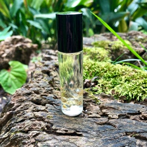 May include: A clear glass roller bottle with a black cap, filled with a light yellow liquid. The bottle is sitting on a piece of weathered wood.