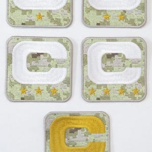 May include: Five embroidered patches with a military theme. Four patches feature a white "C" on a camouflage background, with gold stars below. The fifth patch has a gold "C" and gold stars.