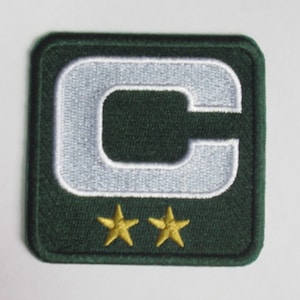 Puede incluir: Parche de fieltro verde con una letra "C" bordada en blanco y dos estrellas bordadas en oro.