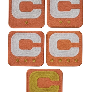 May include: Five orange embroidered patches with a white letter "C" design. Each patch has a square shape and features gold star accents. The bottom patch has a gold "C".