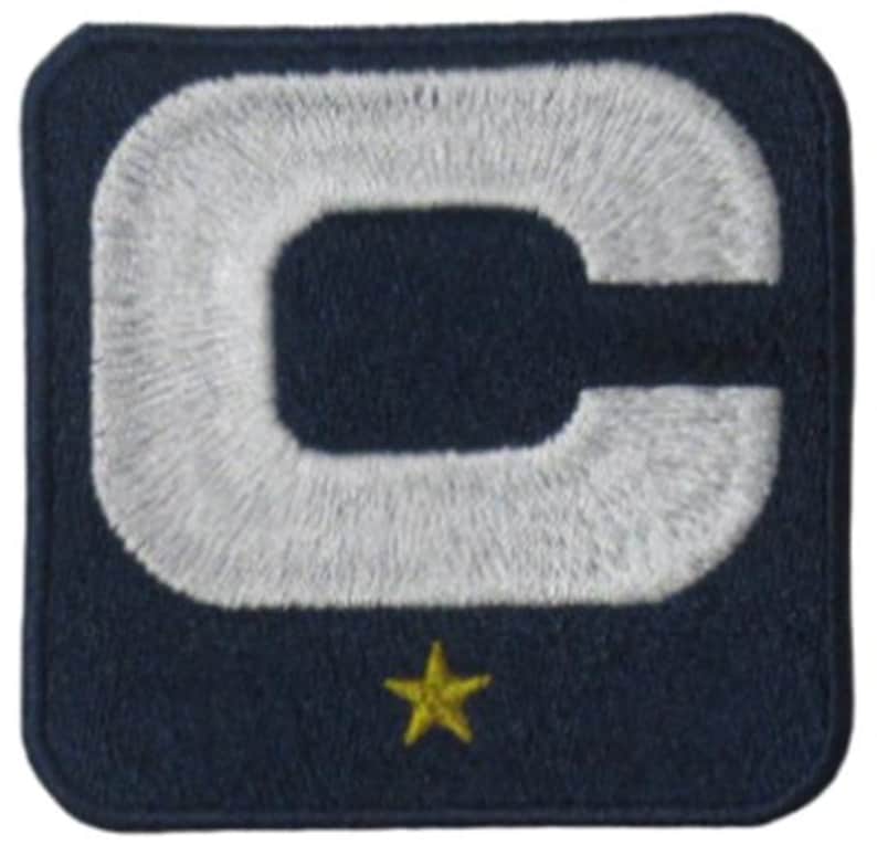 May include: Embroidered patch featuring a large white letter "C" on a navy blue background. A small gold star is positioned below the letter. The patch has a square shape with rounded corners.