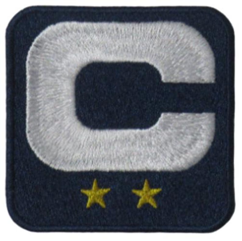 May include: Embroidered patch with a navy blue background and a large, white, stylized letter "C". Two small, yellow stars are positioned below the letter. The patch has a square shape with rounded corners.