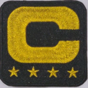 Op de afbeelding: Een geborduurde patch in zwart en goud met een grote letter "C" en vier sterren.