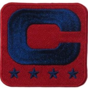 May include: A square, embroidered patch with a red background. A large, navy blue letter "C" is centered on the patch. Below the "C" are four navy blue stars. The patch has a stitched border.