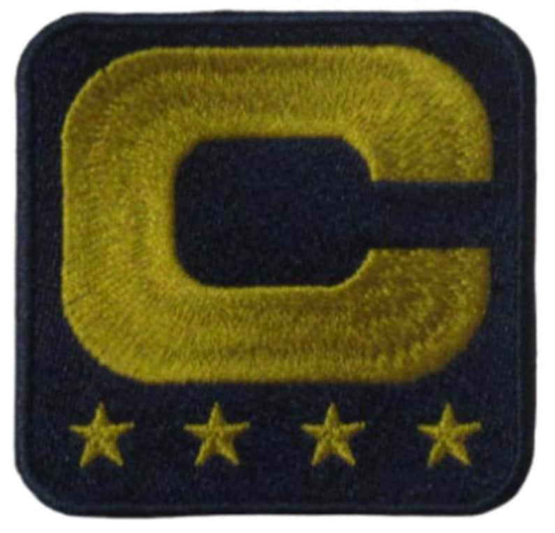 May include: Embroidered patch featuring a large gold letter "C" on a navy blue square. Below the letter are four gold stars. The patch has a textured appearance, suggesting it is made of fabric.