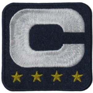 May include: Embroidered patch with a navy blue background. A large, white, capital letter "C" is centered, with a white embroidered outline. Four gold stars are embroidered along the bottom edge. The patch is square with rounded corners.