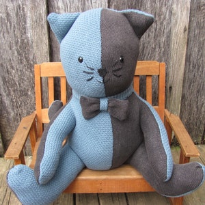 May include: A blue and black knitted cat plush toy wearing a black bow tie sits on a wooden bench.