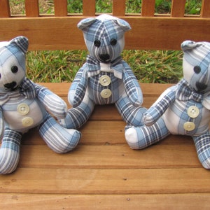 May include: Three blue and white plaid teddy bears with white buttons and bow ties sitting on a wooden bench.