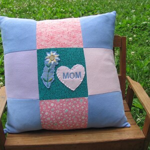 May include: A blue and pink patchwork pillow with a heart-shaped applique that says "MOM" and a flower design.