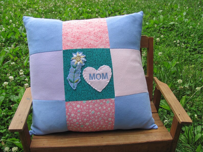 May include: A blue and pink patchwork pillow with a heart-shaped applique that says "MOM" and a flower design.