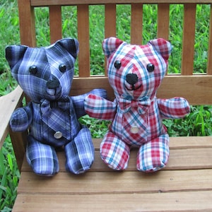 May include: Two plaid fabric teddy bears sitting on a wooden bench. One bear is blue and black plaid, the other is red and white plaid. Both bears have black eyes and a black nose.
