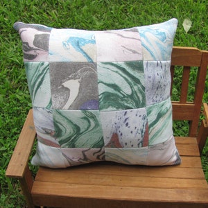 May include: A patchwork pillow with a marbled design in shades of green, blue, pink, and gray. The pillow is made of fabric squares sewn together.