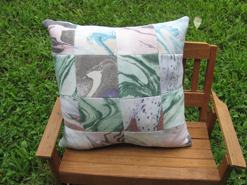 May include: A patchwork pillow with a marbled design in shades of green, blue, pink, and gray. The pillow is made of fabric squares sewn together.