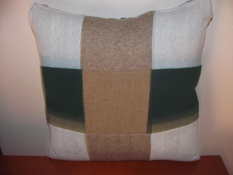 May include: A patchwork pillow with a brown, white, and green color scheme. The pillow is made of different fabrics, including a herringbone pattern.