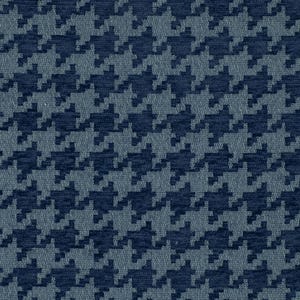 May include: Close-up of a fabric with a classic houndstooth pattern. The design features a repeating pattern of dark navy blue and light blue-grey shapes. The fabric has a textured appearance, suggesting a woven material.