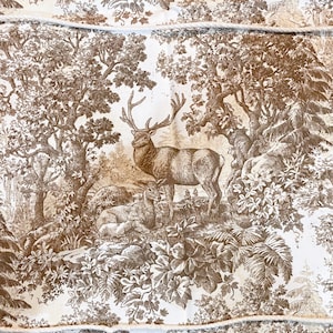 May include: A white fabric featuring a brown monochromatic toile de jouy print of a forest scene with a standing stag and a resting deer. A thick, light-colored twisted rope is arranged in a rectangular shape over the center of the fabric.