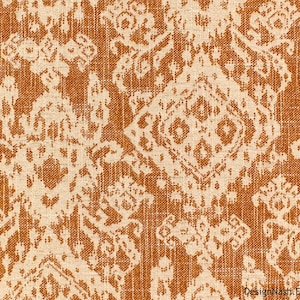 May include: Close-up of a textured fabric with a repeating pattern in shades of orange and cream. The design features stylized floral and geometric shapes, creating a vintage or bohemian aesthetic. The fabric's weave is visible, adding to its tactile appearance.