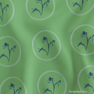 May include: Green fabric with a repeating pattern of navy blue floral illustrations within white circles. The fabric has a slightly textured appearance, with a soft, flowing drape. The design is simple and elegant.
