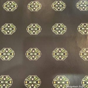 May include: Dark brown background with a repeating pattern of stylized floral designs. Each design features a central white shape surrounded by green and yellow accents, creating a symmetrical, decorative motif.