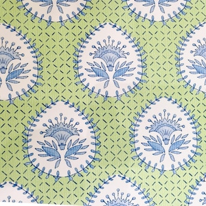 May include: A green fabric with a white and blue floral pattern. The pattern features a repeating design of stylized flowers with blue petals and leaves.