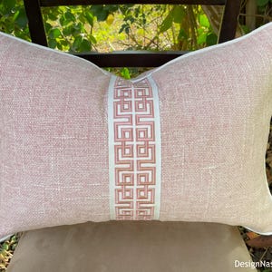 May include: A pink and white throw pillow with a geometric pattern down the center. The pillow is made of a soft, textured fabric.