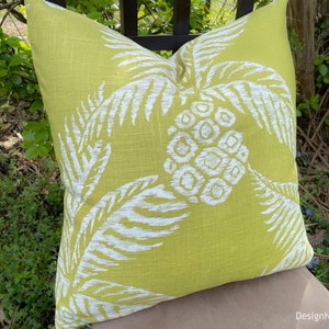 May include: A green pillow with a white palm leaf pattern. The pillow is made of a soft, textured fabric.