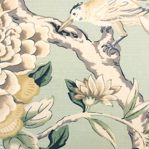 May include: A green fabric with a floral pattern featuring a bird perched on a branch. The flowers are in shades of white, yellow, and brown. The bird is white with yellow and blue accents.