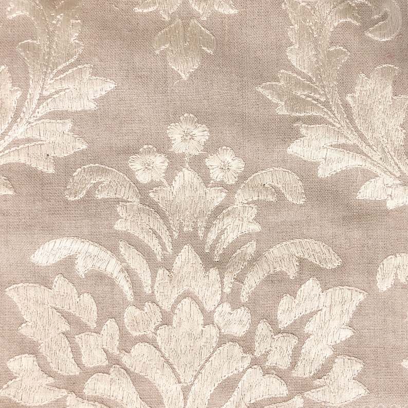 Peut inclure: Un tissu beige avec un motif floral brod&eacute; blanc. Le motif pr&eacute;sente un dessin r&eacute;p&eacute;titif de feuilles et de fleurs.
