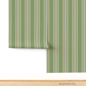 May include: Green and white striped wallpaper with thin orange and gray accent stripes. The wallpaper is partially rolled, revealing the pattern. The bottom of the image shows a wooden surface. The Etsy shop name, DesignNash.Etsy, is visible.