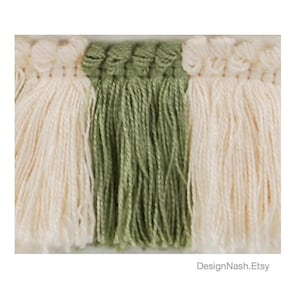 May include: Close-up of a decorative textile with three vertical sections. The outer sections are cream-colored with a fringed edge, and the center section is olive green with a similar fringed edge. The textile is likely used for home decor.