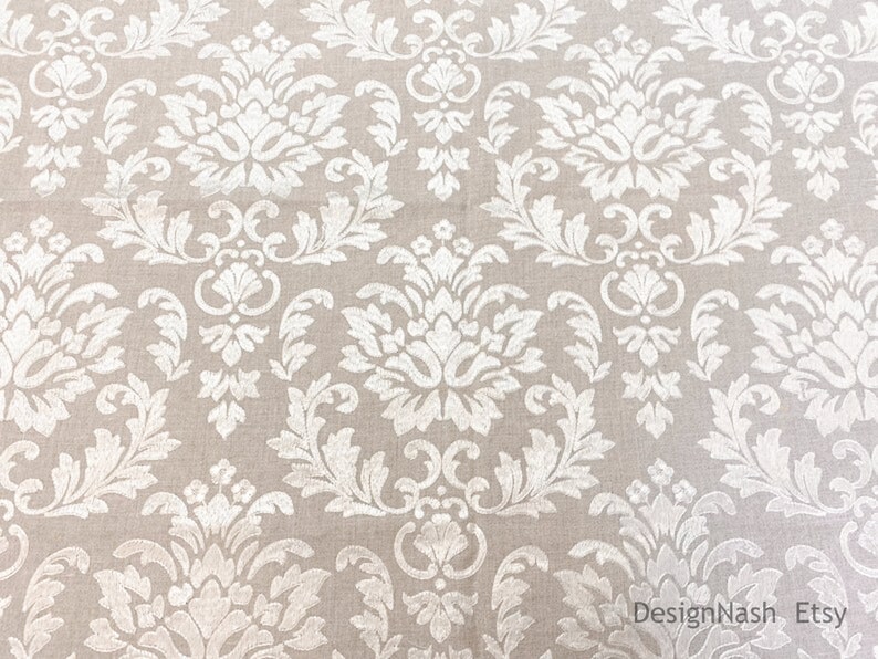 Peut inclure: Tissu beige avec un motif damass&eacute; blanc. Le motif pr&eacute;sente un dessin r&eacute;p&eacute;titif de fleurs et de feuilles stylis&eacute;es.
