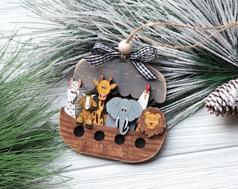 May include: Wooden Noah's Ark ornament featuring a brown ark with various animal figures, including a giraffe, elephant, and lion. The ark has the text "Noah's Ark" engraved on it. A black and white checkered ribbon and a wooden bead are attached for hanging.
