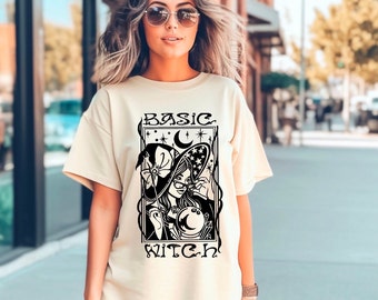 Könnte beinhalten: Ein beiges T-Shirt mit einem schwarzen Aufdruck einer Hexe mit einer Kristallkugel und dem Text "BASIC WITCH" darauf.