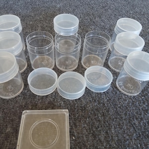 Puede incluir: Un conjunto de recipientes de plástico transparente con tapas blancas. Los recipientes son cilíndricos y de diferentes alturas. Algunos están abiertos, otros cerrados. También hay una funda cuadrada de plástico transparente con una hendidura circular.