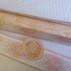 May include: A box of Simple Pleasures rose scented drawer liners containing six 16 inch by 24 inch sheets. The packaging features a floral pattern with pink and yellow roses on a cream background, matching the oval label on the front of the box.