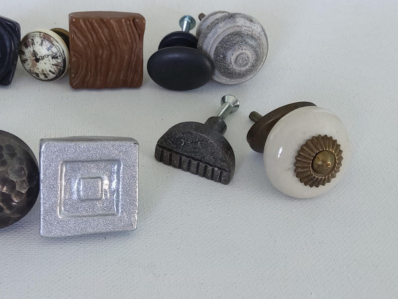 May include: Assortment of decorative cabinet knobs in various styles and materials, including wood, metal, and ceramic. The knobs feature different shapes, patterns, and finishes.