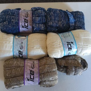 May include: An assortment of yarn skeins in various colors. The top row features blue and white speckled yarn, the middle row has cream-colored yarn, and the bottom row displays metallic gold yarn. Each skein is labeled with a brand name.