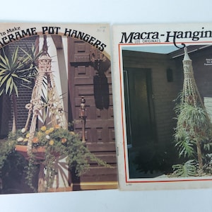 May include: Two vintage macrame pot hanger pattern books. The book on the left is titled "Easy to Make Macrame Pot Hangers" and features a macrame pot hanger with a plant hanging from it. The book on the right is titled "Macra-Hangings Lee Originals" and features a macrame pot hanger with a plant hanging from it.