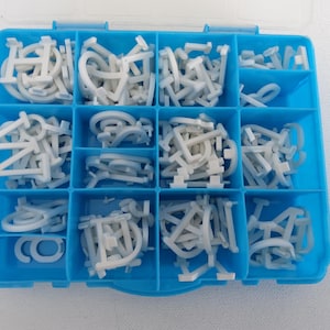 May include: A blue plastic organizer filled with white, rubbery letter and number shapes. The shapes are in various fonts and sizes, perfect for crafting or educational projects. The organizer has a clear lid.