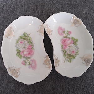 May include: Two white porcelain half-moon shaped dishes with gold trim and pink rose floral designs.