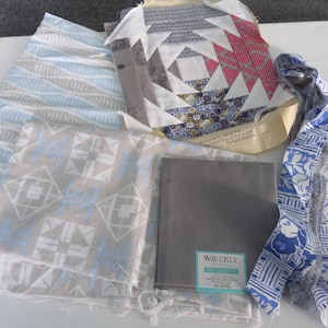 May include: Assortment of fabric pieces in various patterns and colors. Includes a gray square, a blue and white patterned ribbon, and several fabric squares with geometric designs in blue, white, and gray. One piece has a label that says "WAVERLY".